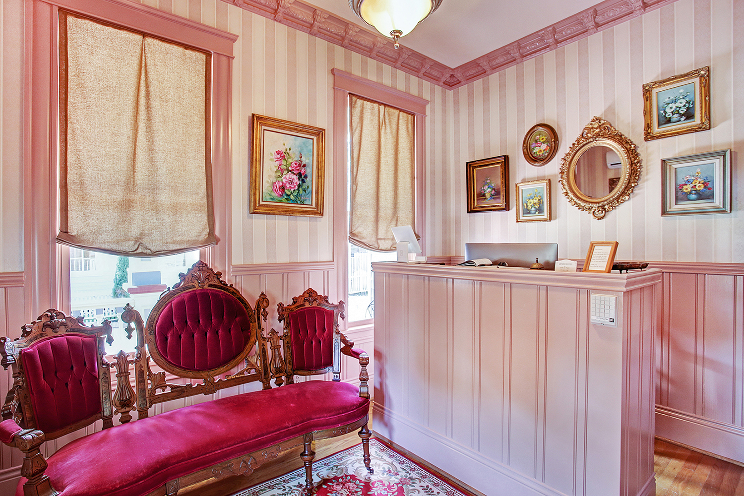 A lobby with a red velvet bench, striped wallpaper, and framed artwork.